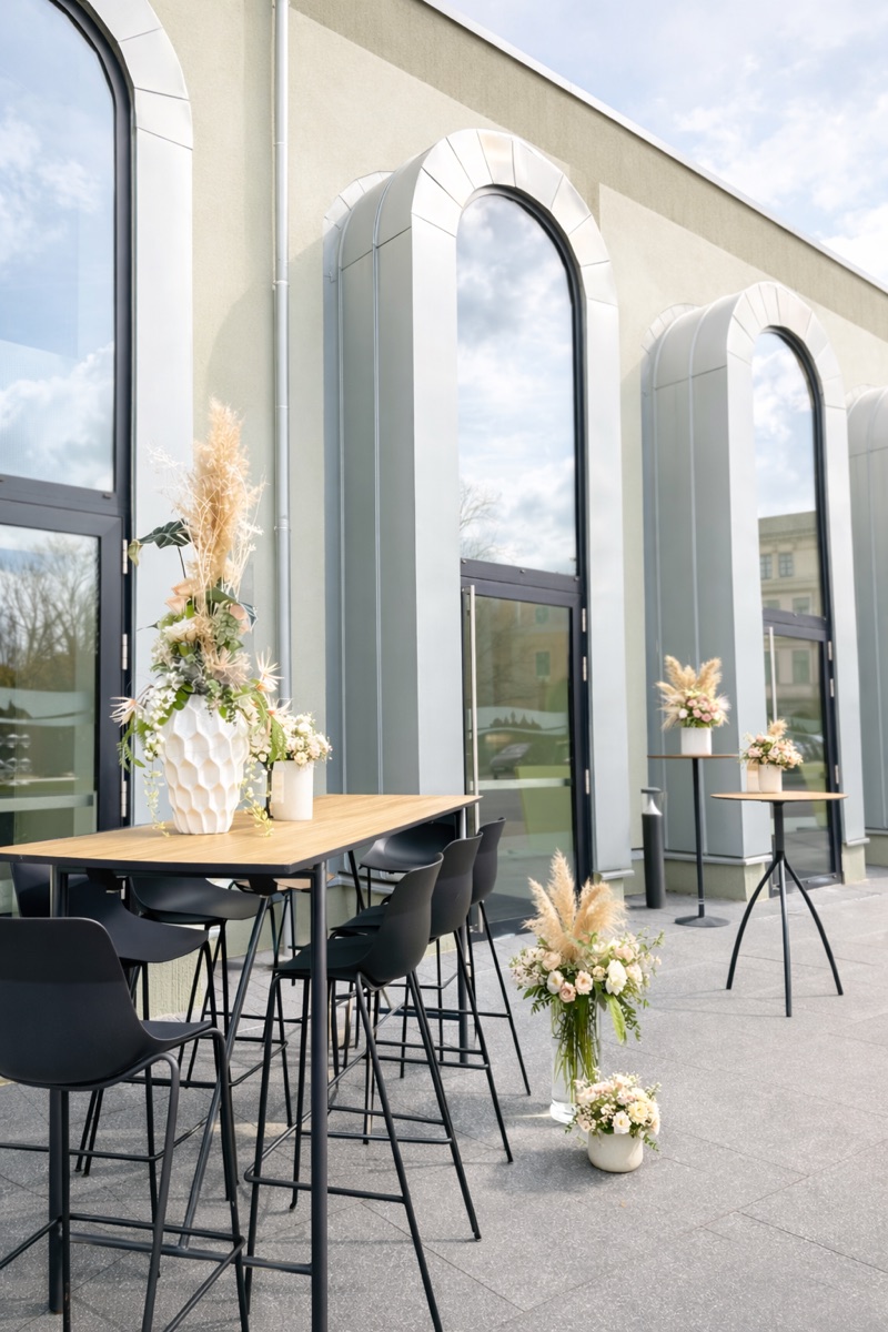 Außenterrasse mit Blumenschmuck vor den Bogenfenstern